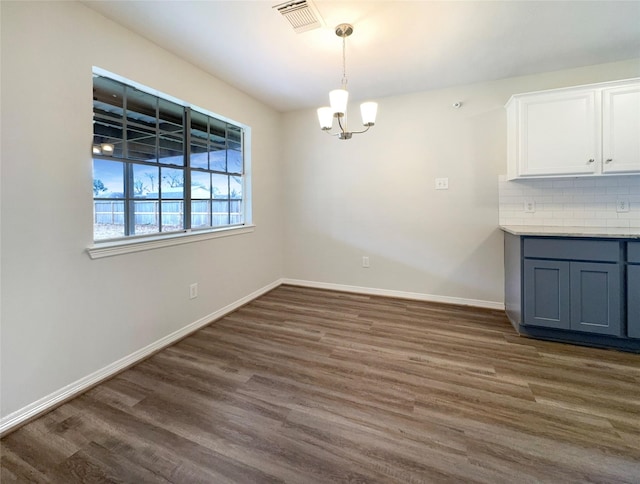 unfurnished dining area with dark wood-type flooring and an inviting chandelier