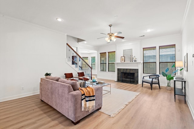 living room with ceiling fan, ornamental molding, a fireplace, and light hardwood / wood-style floors