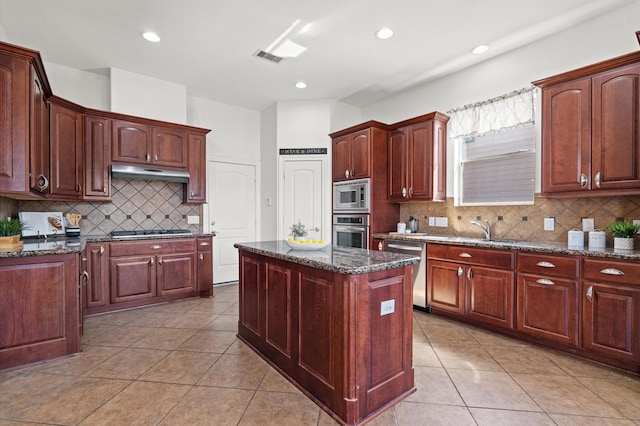 kitchen with dark stone countertops, decorative backsplash, a center island, light tile patterned floors, and stainless steel appliances