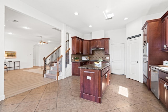 kitchen featuring light tile patterned flooring, stainless steel appliances, a kitchen island, dark stone counters, and backsplash