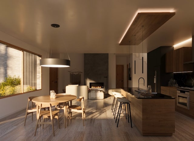 kitchen featuring a breakfast bar area, light wood-type flooring, gas cooktop, wall oven, and a fireplace