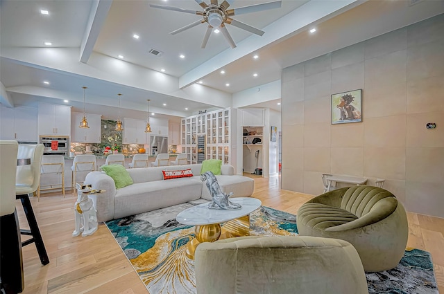 living room with beamed ceiling, ceiling fan, tile walls, and light wood-type flooring