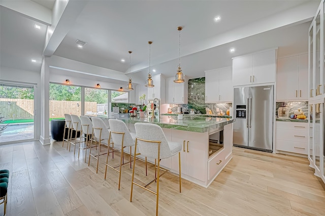 kitchen with hanging light fixtures, high quality fridge, white cabinets, a kitchen bar, and a large island with sink