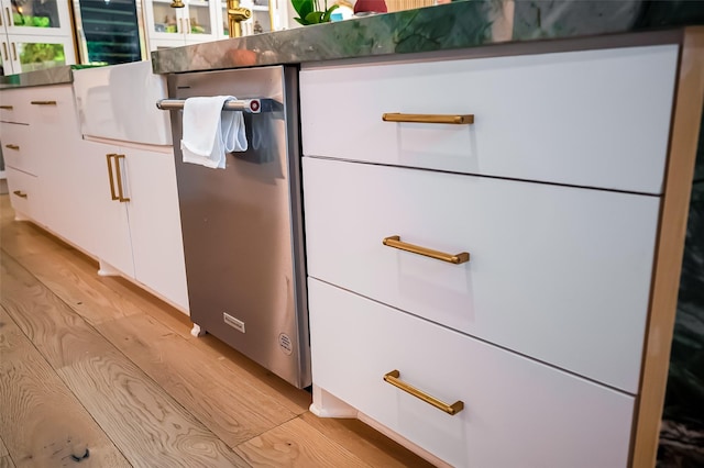 room details featuring white cabinetry, stainless steel dishwasher, and light hardwood / wood-style floors