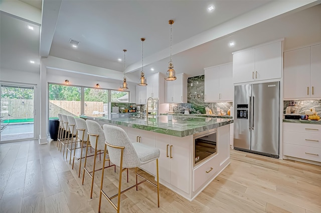 kitchen with high end fridge, backsplash, a spacious island, white cabinets, and decorative light fixtures