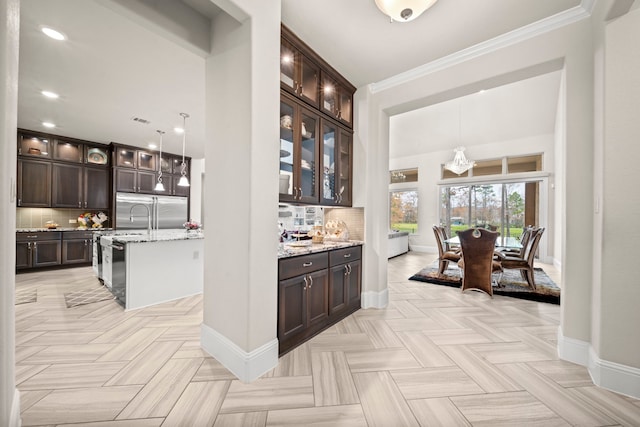 kitchen with dark brown cabinetry, stainless steel built in refrigerator, light stone counters, tasteful backsplash, and decorative light fixtures