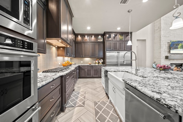 kitchen featuring appliances with stainless steel finishes, pendant lighting, decorative backsplash, light parquet floors, and dark brown cabinetry