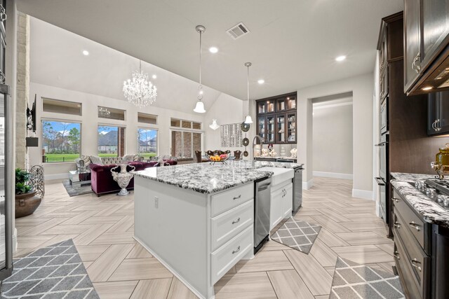 kitchen with dark brown cabinetry, decorative light fixtures, light stone countertops, a kitchen island with sink, and white cabinets