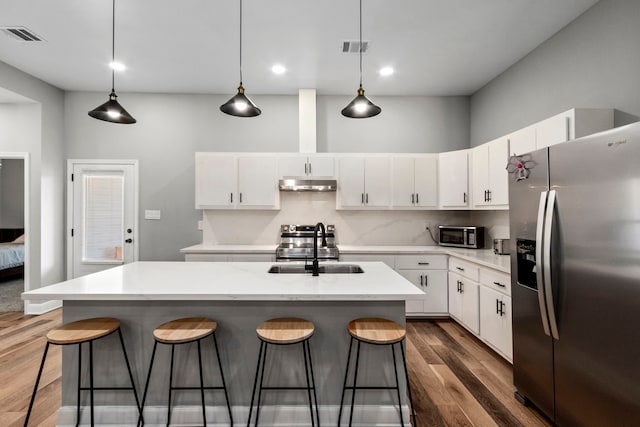 kitchen with a center island with sink, light countertops, appliances with stainless steel finishes, white cabinetry, and under cabinet range hood