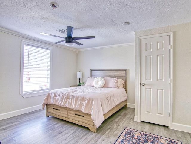 bedroom with hardwood / wood-style flooring, ornamental molding, ceiling fan, and a textured ceiling