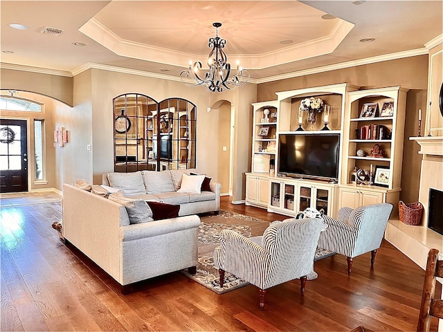 living room featuring an inviting chandelier, wood-type flooring, a tray ceiling, and a premium fireplace