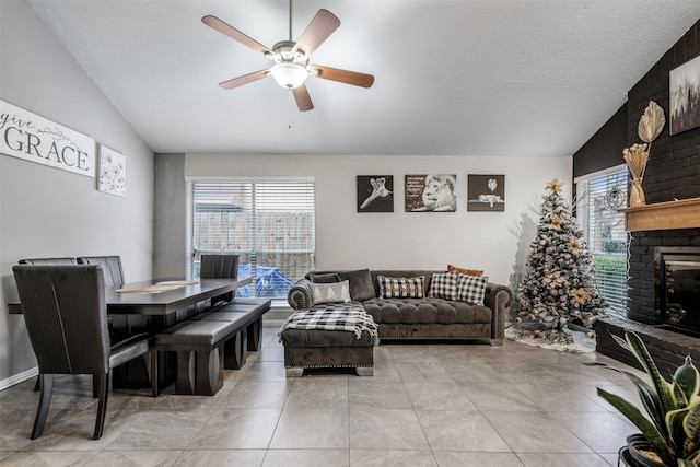 tiled living room with ceiling fan, lofted ceiling, a textured ceiling, and a fireplace