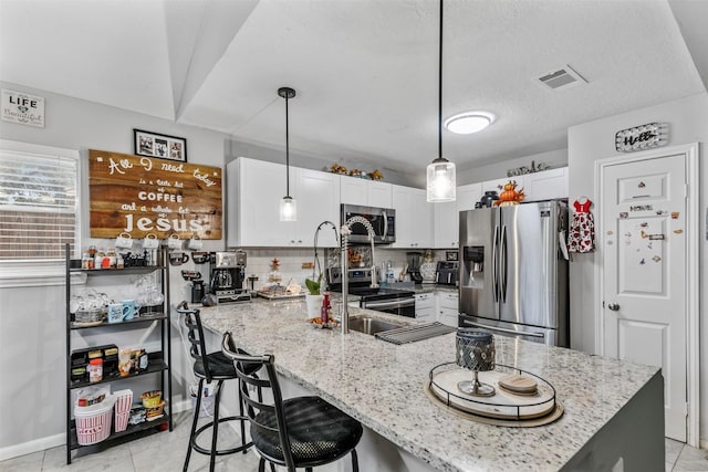 kitchen with appliances with stainless steel finishes, pendant lighting, white cabinets, decorative backsplash, and light stone counters