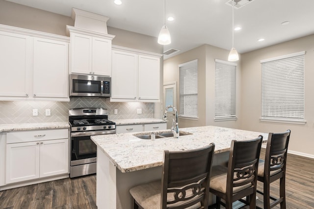 kitchen featuring sink, appliances with stainless steel finishes, hanging light fixtures, white cabinets, and a center island with sink