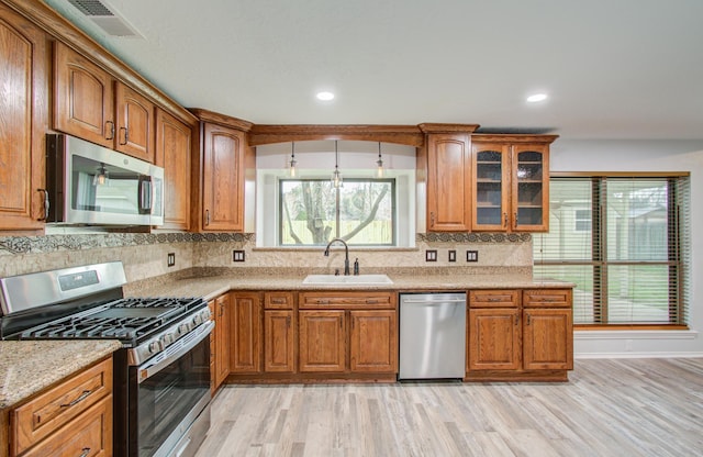 kitchen with sink, appliances with stainless steel finishes, light stone countertops, light hardwood / wood-style floors, and decorative backsplash