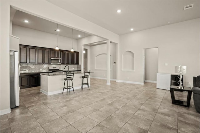 kitchen featuring sink, a breakfast bar, appliances with stainless steel finishes, tasteful backsplash, and a center island with sink