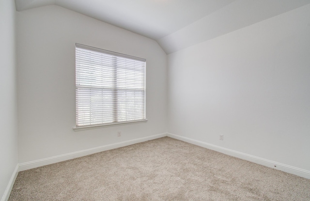 carpeted empty room featuring baseboards and lofted ceiling