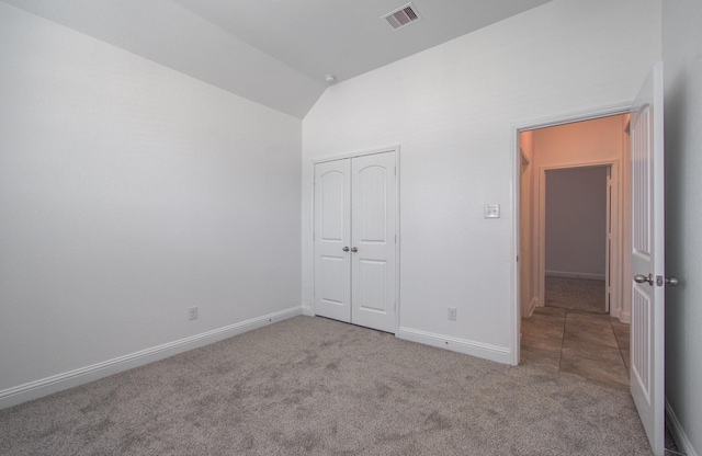 unfurnished bedroom featuring carpet, baseboards, lofted ceiling, visible vents, and a closet