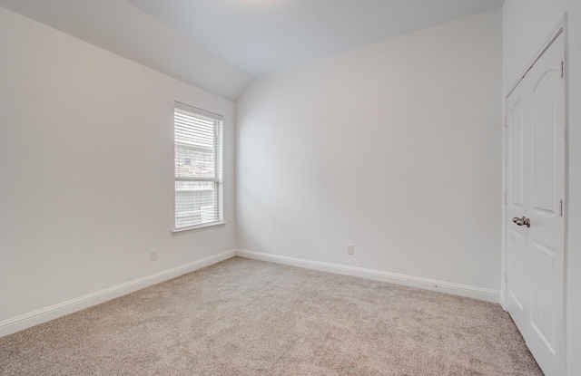 unfurnished room with baseboards, vaulted ceiling, and light carpet