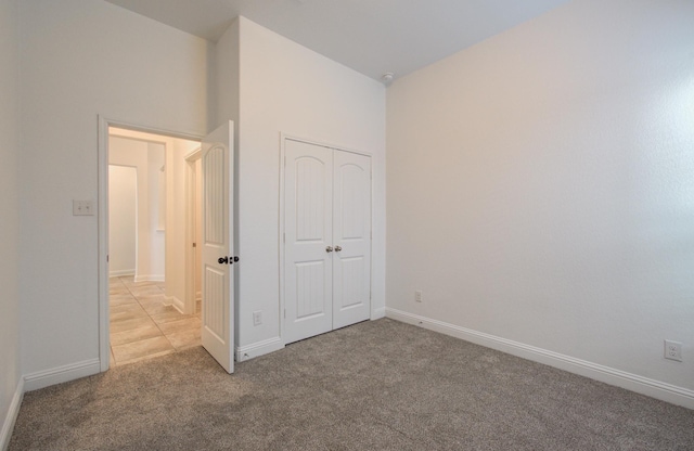 unfurnished bedroom featuring baseboards, light colored carpet, and a closet