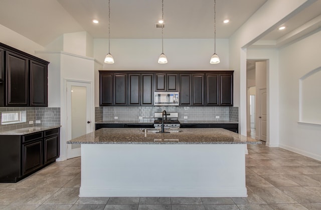 kitchen featuring appliances with stainless steel finishes, a sink, a kitchen island with sink, dark stone counters, and tasteful backsplash