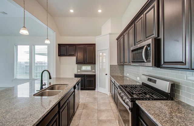 kitchen with dark brown cabinetry, appliances with stainless steel finishes, a sink, stone countertops, and tasteful backsplash