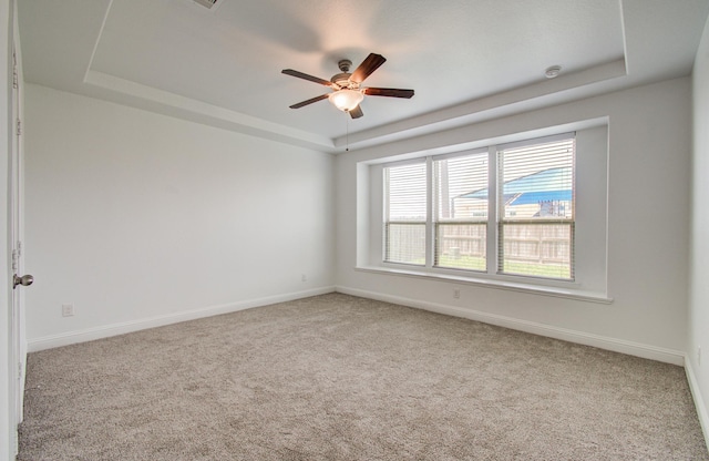 carpeted spare room featuring baseboards, a tray ceiling, and ceiling fan