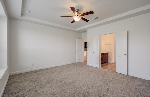 unfurnished bedroom featuring visible vents, a raised ceiling, baseboards, ensuite bathroom, and light carpet
