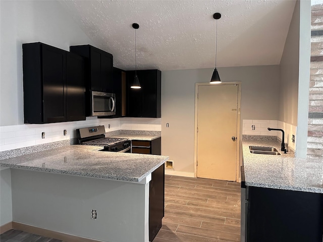 kitchen with appliances with stainless steel finishes, decorative light fixtures, sink, kitchen peninsula, and light hardwood / wood-style flooring