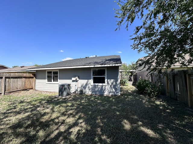 rear view of house with central AC unit and a lawn