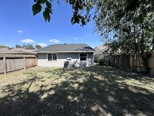 rear view of property with central AC unit and a lawn