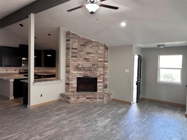 unfurnished living room with hardwood / wood-style floors, a fireplace, vaulted ceiling with beams, ceiling fan, and a textured ceiling