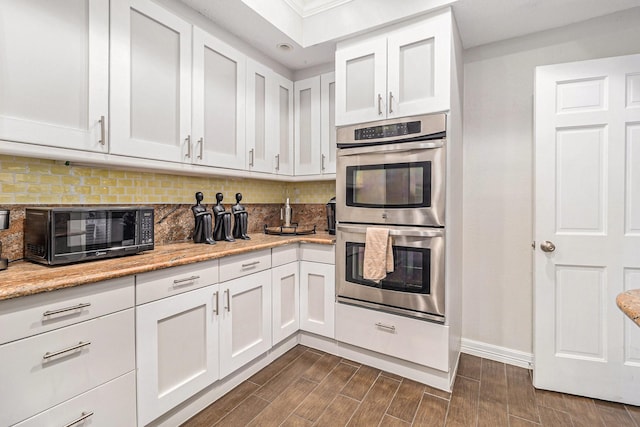 kitchen featuring tasteful backsplash, light stone counters, white cabinets, and double oven