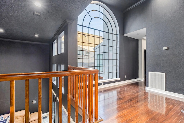 hall with hardwood / wood-style flooring, crown molding, and a textured ceiling