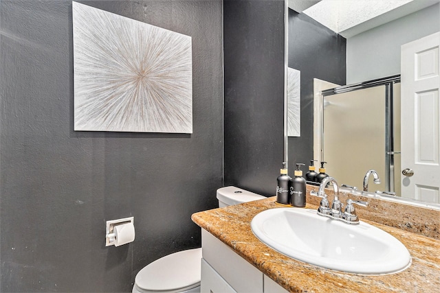 bathroom with vanity, a skylight, a shower with shower door, and toilet