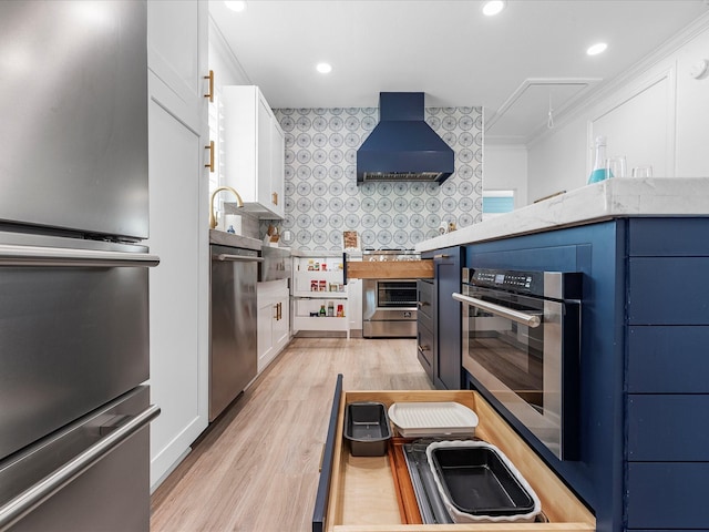 kitchen with wall chimney range hood, crown molding, stainless steel appliances, white cabinets, and decorative backsplash