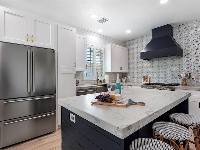 kitchen featuring white cabinetry, wall chimney range hood, a kitchen island, and appliances with stainless steel finishes