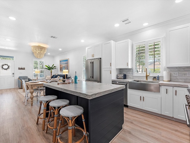 kitchen with sink, light hardwood / wood-style flooring, appliances with stainless steel finishes, white cabinetry, and a center island