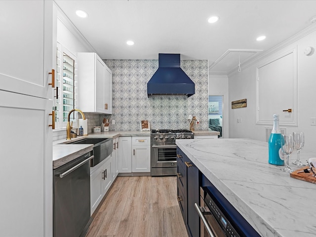 kitchen with appliances with stainless steel finishes, sink, white cabinets, decorative backsplash, and wall chimney exhaust hood