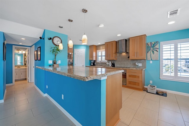 kitchen with pendant lighting, backsplash, plenty of natural light, and wall chimney exhaust hood