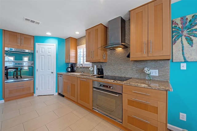 kitchen featuring sink, backsplash, stainless steel appliances, light stone countertops, and wall chimney range hood