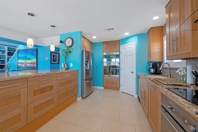 kitchen featuring stainless steel appliances, sink, light stone counters, and decorative light fixtures