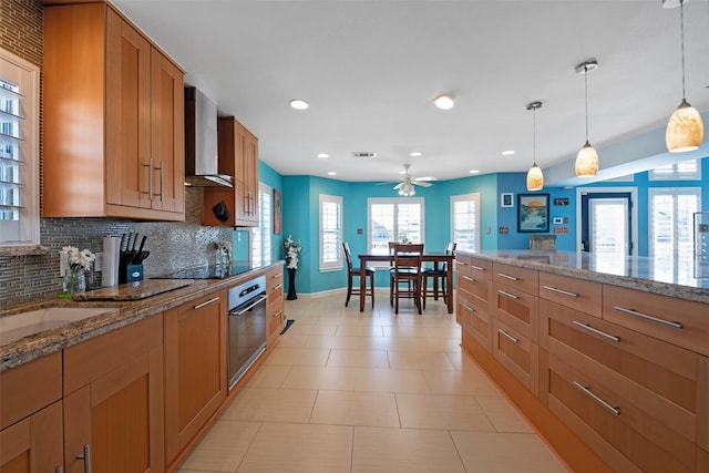 kitchen with decorative light fixtures, decorative backsplash, stainless steel oven, light stone counters, and wall chimney exhaust hood