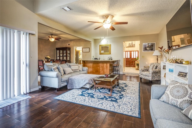 living room with dark wood-type flooring, ceiling fan, and a textured ceiling