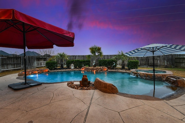 pool at dusk featuring an in ground hot tub, pool water feature, and a patio area