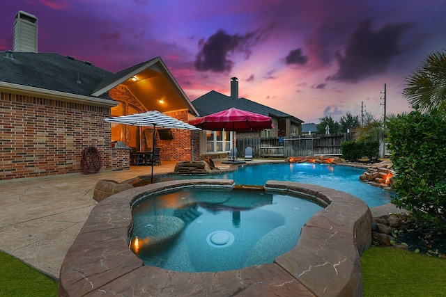 pool at dusk with a patio area and an in ground hot tub