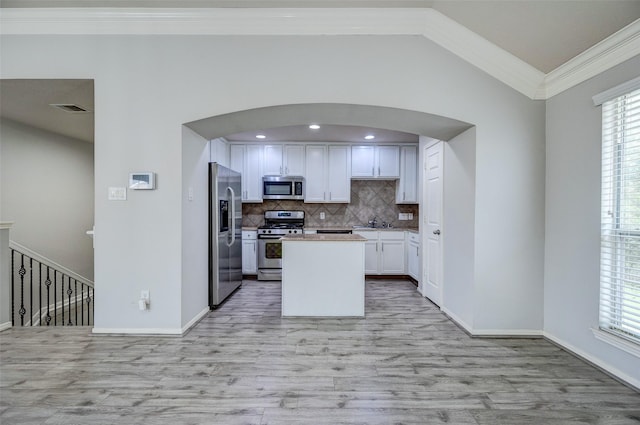 kitchen featuring vaulted ceiling, white cabinets, decorative backsplash, ornamental molding, and stainless steel appliances