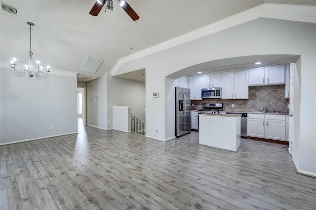 kitchen featuring appliances with stainless steel finishes, lofted ceiling, white cabinets, decorative backsplash, and hanging light fixtures