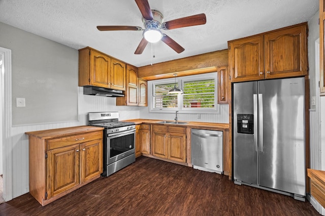 2817 John St, La Marque, TX 77568 - kitchen featuring under cabinet range hood, brown cabinets, a sink, dark wood finished floors, and appliances with stainless steel finishes