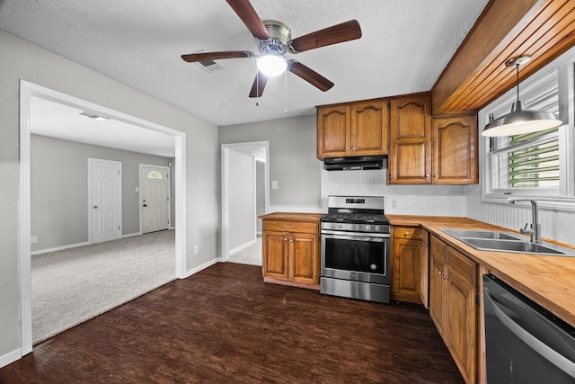 2817 John St, La Marque, TX 77568 - kitchen with brown cabinetry, appliances with stainless steel finishes, a sink, dark wood-style floors, and under cabinet range hood